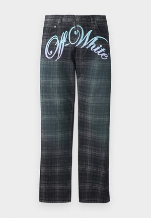 Jeune homme debout, portant un t-shirt noir avec un petit logo et un pantalon gris à carreaux avec un grand texte « Off-White » sur le devant.