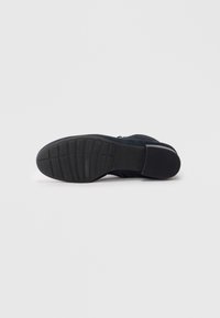 Bottine noire en daim avec une semelle en caoutchouc texturée, dotée d'une fermeture éclair sur le côté et d'un design minimaliste. Surface lisse avec des détails de couture subtils.