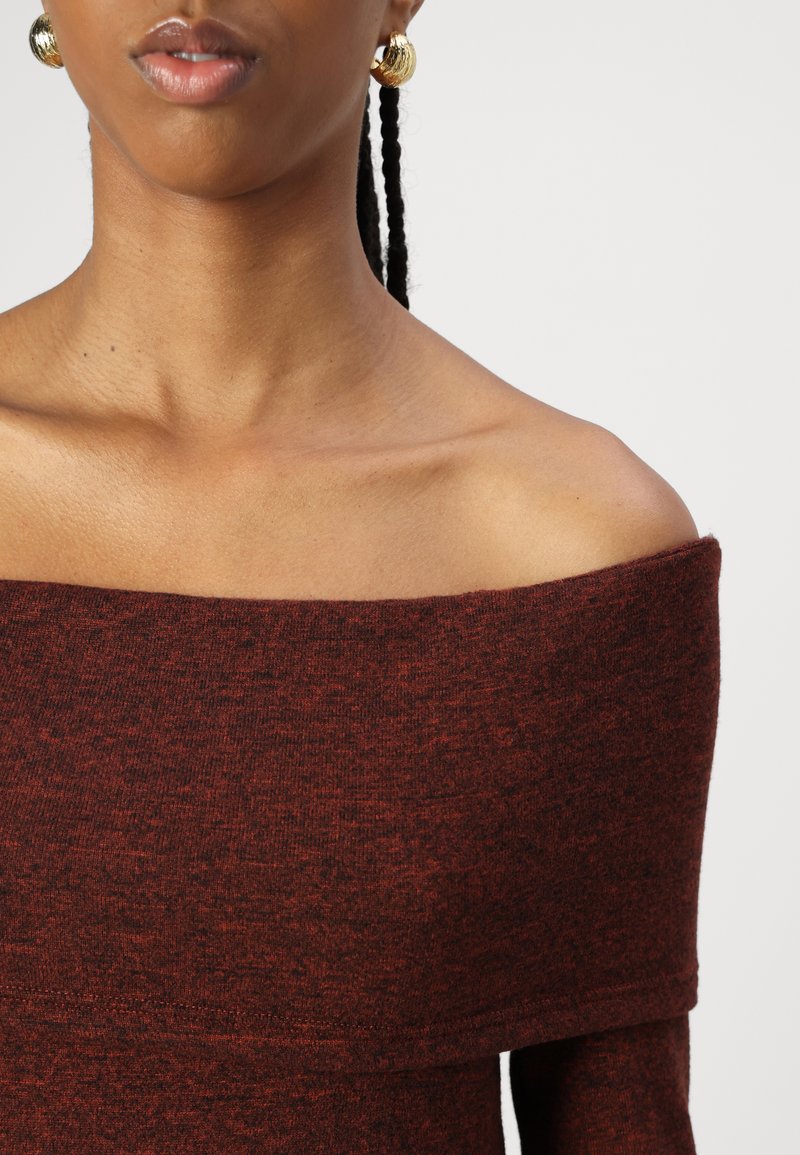 Top marrón de punto con hombros al descubierto y un acabado texturizado. Se ven pendientes de aro dorados que complementan la paleta de colores del atuendo.