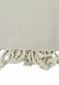 Helles Creme-gewebtes Textil mit der strukturierten oberen Hälfte, versehen mit gedrehtem Fransen am unteren Ende, welches die taktile Detailverarbeitung erhöht.