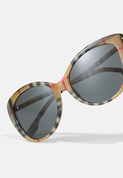 Lunettes de soleil Burberry avec monture oversize en œil de chat. Beige transparent avec un motif à carreaux noir et rouge ; verres gris foncé. Texture lisse.