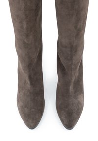 Stivali alti in suede marrone con punte affusolate, visti dall'alto su uno sfondo bianco.