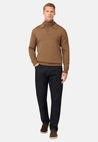 Brauner gerippter Pullover mit Kragen, kombiniert mit dunklen Jeanshosen und braunen Slippern. Schlichtes, modernes Design mit körpernahem Schnitt.