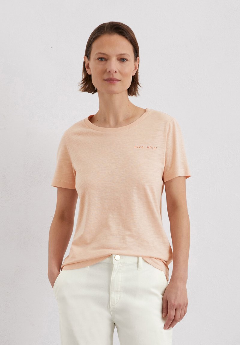 Light peach crew neck t-shirt with short sleeves, featuring subtle texture and small red embroidery saying "nice, nice!" on the chest.