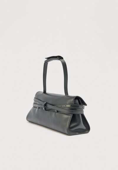 Μαύρη δερμάτινη τσάντα χειρός με δομημένο σχήμα τραπεζοειδούς, ρυθμιζόμενο λουράκι με αγκράφα και μονή λαβή για τον ώμο σε μονόχρωμο φόντο.