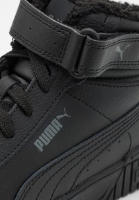 Czarne skórzane trampki o teksturowanej powierzchni, z wyściełanym kołnierzem, sznurowanym przodem i paskiem na rzep. Logo Puma w kolorze szarym.