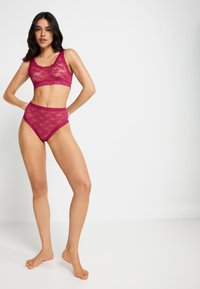 Magenta kanten bralette en hooggedragen slipset met een bloemenpatroon, gekartelde randen en een doorzichtige textuur.