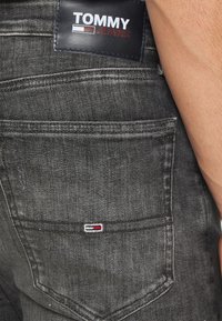 Los vaqueros de mezclilla oscura presentan una etiqueta rectangular de Tommy Jeans en la pretina y un pequeño logotipo bordado en el bolsillo trasero.