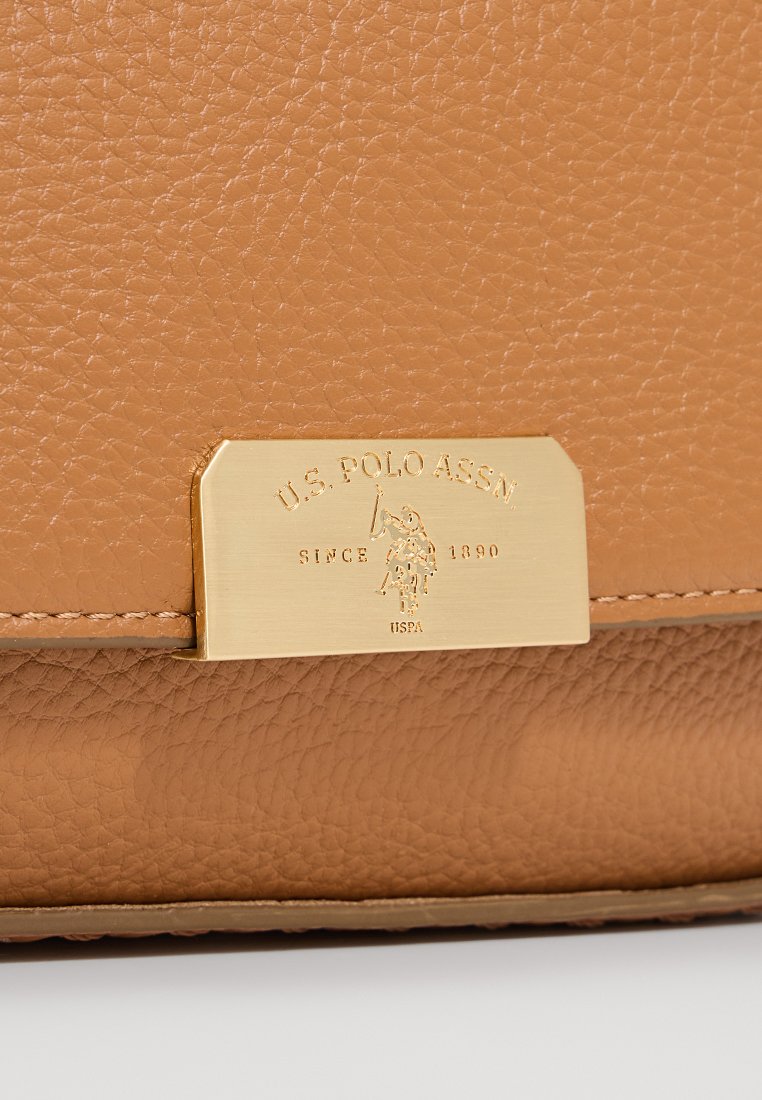 Sac à main en cuir texturé tan avec une plaque en métal doré portant un texte gravé et un emblème. Les coutures sont visibles le long des bords.