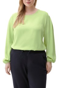 Lime green pitkähihaine pusero, jossa on pyöreä pääntie, pehmeä rakenne ja rypytetyt hihansuut, yhdistettynä tummansinisiin joustaviin vyötäröhousuihin.