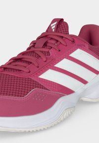 Ροζ αθλητικό παπούτσι με λευκές ρίγες Adidas, επάνω μέρος από διχτυωτό υλικό, ανατομικό πέλμα και υφή στη λευκή σόλα.