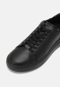 Baskets en cuir noir avec lacets noirs, logo embossé sur le côté et une silhouette élégante à bout arrondi.