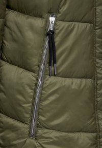 Grön pufferjacka med en silverdragkedja. Har en quiltad design, mjuk textur och svarta snoddar som accentuerar dragkedjan.