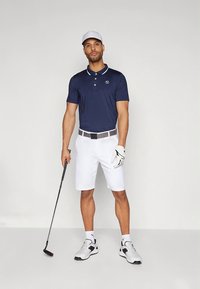 Tmavomodré polo tričko s bielym golierom, biele šortky a sivý opasok. Na nohách biele golfové topánky a na hlave biela čiapka, drž�í golfovú palicu.