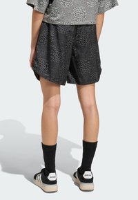 Čierne šortky s leopardím vzorom, voľného strihu a bočnými rozparkami, doplnené o čierne pančuchy po kolená a čierne tenisky s bielymi detailmi.