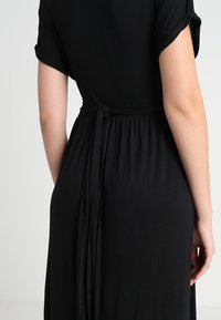 Musta mekko lyhyillä käännetyillä hihoilla, kireä vyötärö pitkästä kangasvyöstä, jossa on pehmeä ja sileä rakenne.