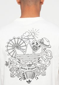 White t-shirt featuring a black line art design on the back, including an Adidas logo, ferris wheel, food items, and musical instruments.