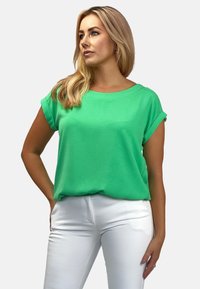 Zielony krótki rękaw bluzka z miękkiego materiału o luźnym kroju, z podwiniętymi rękawami. Połączona z białymi obcisłymi spodniami.