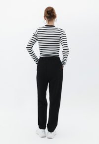 Sorte bukser med elastisk talje og to baglommer, parret med en langærmet skjorte med sort-hvide striber. Hvide sneakers fuldender looket.