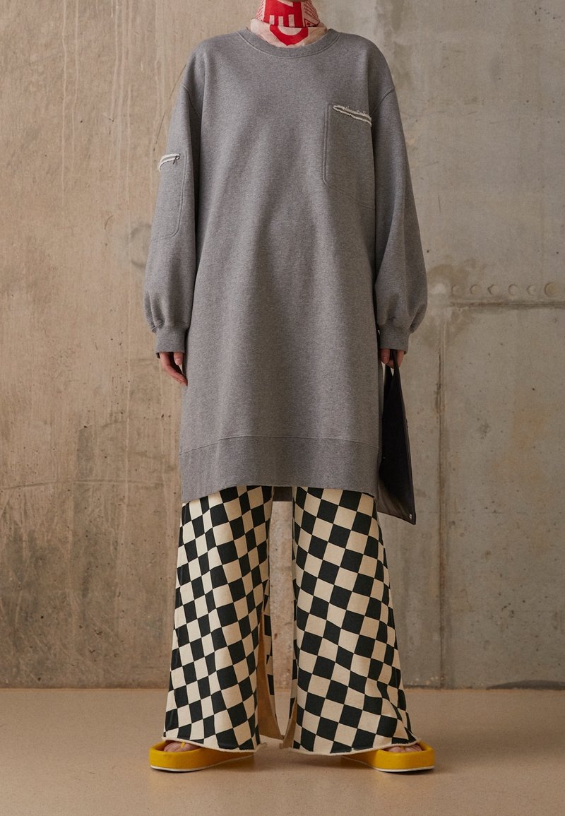 Grå oversized sweatshirt med en framficka och sydda detaljer, kombinerad med vida svartvita rutiga byxor och gula platåskor.