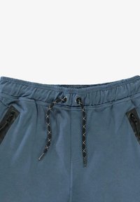 Blauwe broek met elastische tailleband, zwarte en witte trekkoorden en ritssluitingen aan de zijkanten.