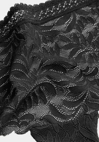 Tessuto in pizzo nero con intricati motivi a foglia, texture trasparente e bordo scallop. Il design presenta una combinazione di aree in rete e solide.