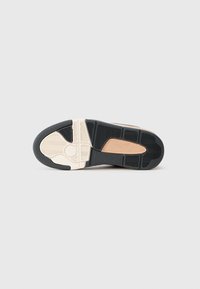 Suela de una zapatilla con colores negro, beige y blanco que presenta patrones de agarre texturizados y un pequeño logotipo grabado.