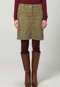 Olijfgroene denim rok met een rechte snit, voorzien van voorkruisen en een knoopsluiting. Gepaard met bruine leren kniehoge laarzen.