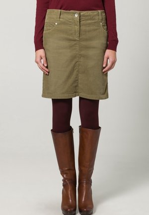 Jupe en denim vert olive avec une coupe droite, dotée de poches avant et d'une fermeture à bouton. Associée à des bottes en cuir marron à hauteur de genoux.