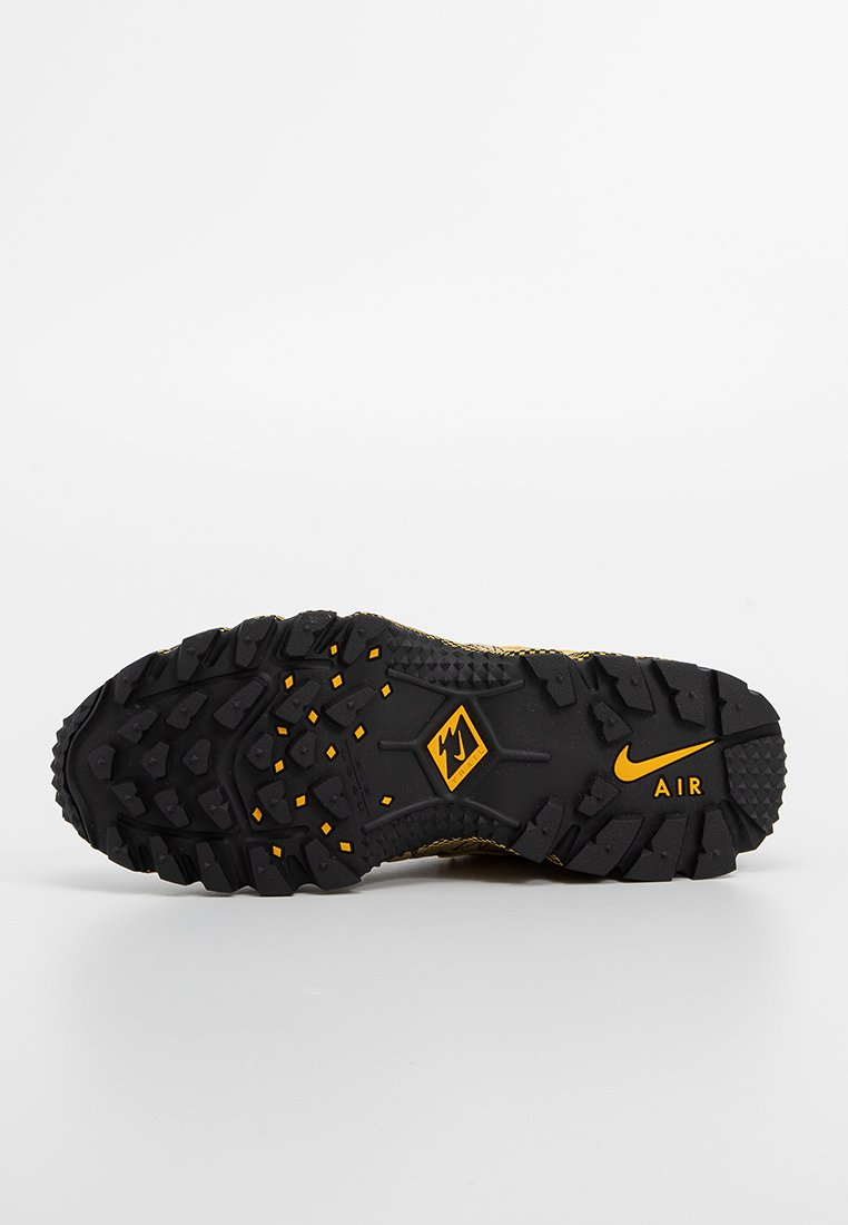 Czarna podeszwa z wielokierunkowymi wypustkami trakcyjnymi, z żółtym logo Nike i pomarańczowymi akcentami. Teksturowana powierzchnia dla lepszej przyczepności.