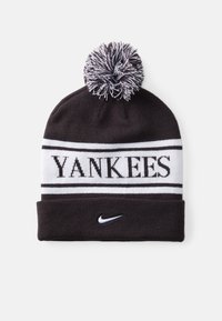 Căciulă tricotată alb-negru cu un pom-pom în vârf, textul "YANKEES" în stil bold și un mic logo alb Nike pe mansetă.