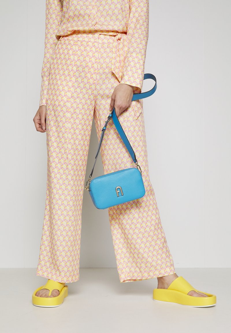 Kostkovaná růžová a žlutá košile a kalhoty, s modrou texturovanou taškou s podpisovým emblémem a žlutými platformovými sandály.