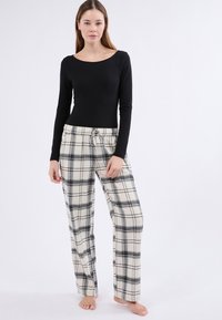 Top negro de manga larga combinado con pantalones de pijama de cuadros beige que presentan líneas grises y una cintura con cordón, hechos de tela suave.