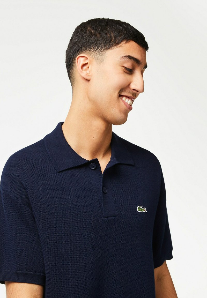Polo shirt marine en coton texturé, avec un col traditionnel, trois boutons et un petit logo crocodile vert sur la poitrine.