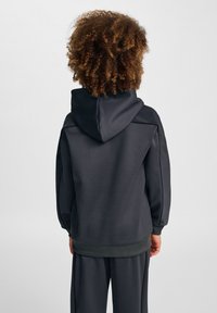 Mörkgrå huvtröja med en slät yta, ribbade avslutningar och en avslappnad passform. Har en enkel design utan synliga logotyper eller mönster.