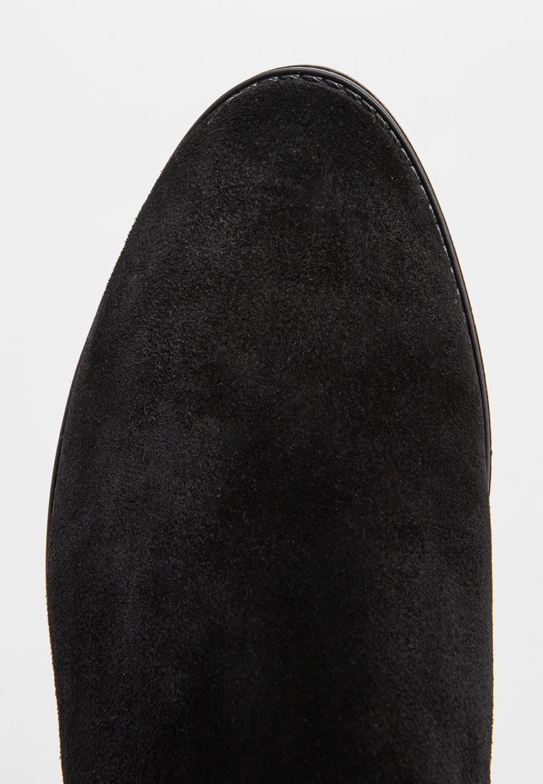 Schwarze Wildleder Stiefelette mit runder Spitze, glatter Textur und kontrastierenden Nähten entlang der oberen Kante.