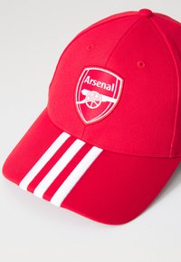 Červená baseballová čiapka s logom Arsenalu v bielej farbe, so štruktúrovanou korunou a tromi bielymi prúžkami na prednej strane šiltu.