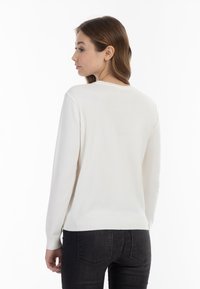 Weißer Pullover mit langen Ärmeln und geripptem Saum, mit Rundhalsausschnitt und glatter Textur, getragen mit dunklen Jeans, von hinten betrachtet.