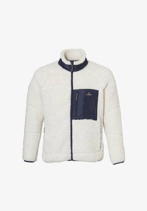Lächelnde Frau trägt eine weiße Fleecejacke mit navyblauer Fronttasche und hellblauer Jeans, steht vor einem weißen Hintergrund.