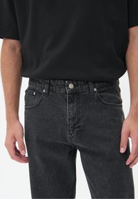 Vaqueros de mezclilla negra con un lavado desgastado, diseño de cinco bolsillos y herrajes plateados. Combinados con una camiseta negra de manga corta y corte holgado.