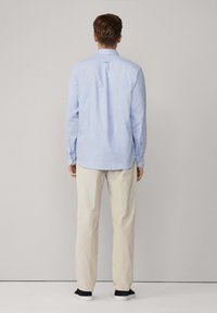 Camisa de manga larga azul claro con cuello abotonado y pliegue en la espalda, combinada con pantalones color crema y zapatillas navy.