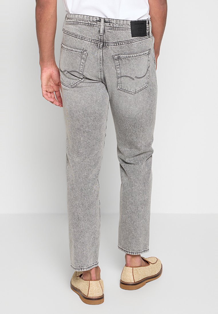 Hellgraue Jeans aus Denim mit Fischgrätmuster, fünf Taschen und einem schwarzen Etikett auf der Rückseite. Kombiniert mit beigen Slippern.