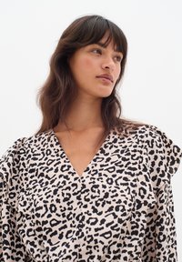 Leopardmönstrad klänning med V-ringning och volangärmar, tillverkad av lättviktsmaterial i beige och svart. Slät textur, avslappnad design.