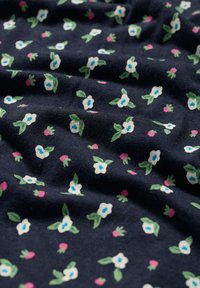 Tamsiai mėlynas audinys su gėlių raštu, kuriame yra baltų gėlių su mėlynais centrais, žalių lapų ir rožinių akcentų, sukuriantis tekstūrinį efektą.