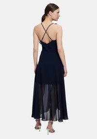 Granatowa sukienka maxi z dopasowanym gorsetem, skrzyżowanymi rami ączkami na plecach oraz zwiewną, przezroczystą spódnicą. Posiada falbaniaste akcenty i zamek błyskawiczny.