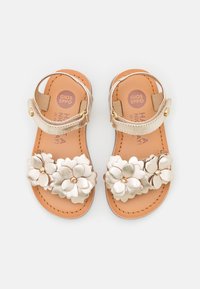 Zlaté metalické sandály se květinovým vzorem, na popruhu jsou tři texturované květiny, hnědá stélka a nastavitelné zapínání na kotníku.