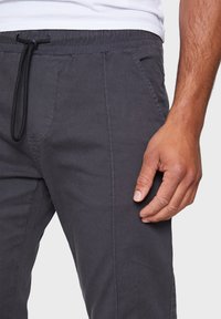 Gray cotton blend pants with an elastic waistband, drawstring, side pockets, and a slightly tapered shape. Textured fabric with stitching details.