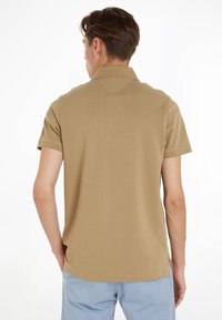 Μπεζ μπλουζάκι πόλο με κοντά μανίκια και κλασικό γιακά, με λεία υφή και άνοιγμα στο τελείωμα στις πλευρές.