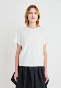 Witte t-shirt van katoen, met korte mouwen en een ronde halslijn, gecombineerd met een zwarte rok. Eenvoudig, klassiek ontwerp met een gladde textuur.