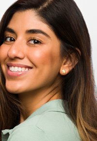 Orecchini d'oro a forma di coniglio, indossati da una donna con lunghi capelli scuri e una camicia colletto verde menta, mentre sorride su uno sfondo chiaro.